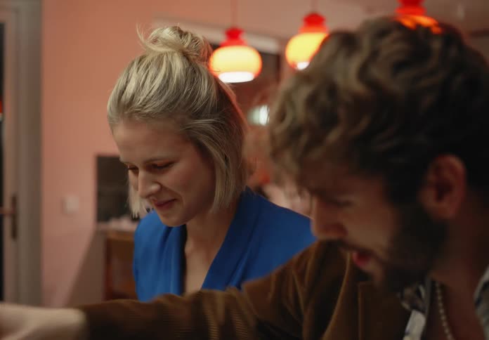 A man is sitting next to a woman at a table as he holds a piece of bread he is eating as he speaks
