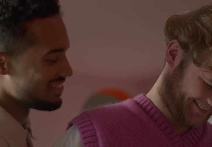 Two men laughing and smiling and loking romantically at eahc other while preparing bread