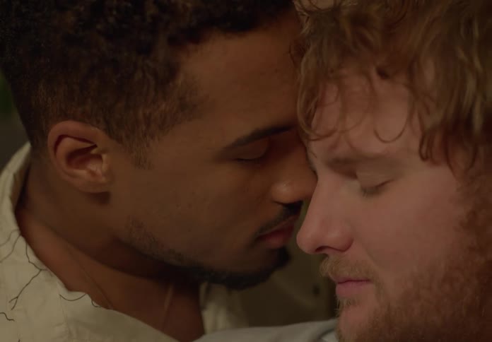 Two men sit closely together nuzzling each other