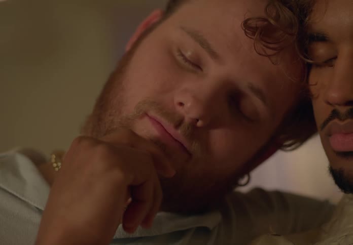 A male couple is falling asleep while one strokes the other ones face