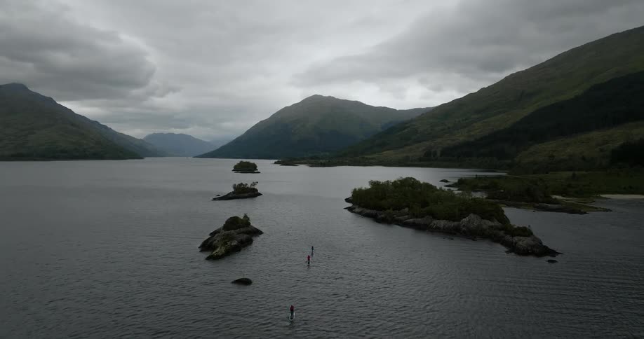 A huge lake is shown with several rocks that have grass on them and the mountains in the background