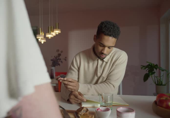 Man with beige sweatshirt sitting at table reads a book in room