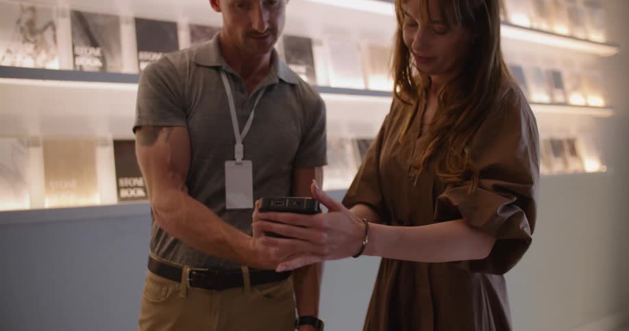 A man and a woman use a pos device while standing in front of an illuminated wall