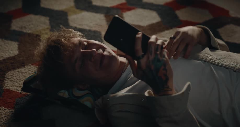 A man is lying on the floor with a pillow under his head as he texts on his cell phone