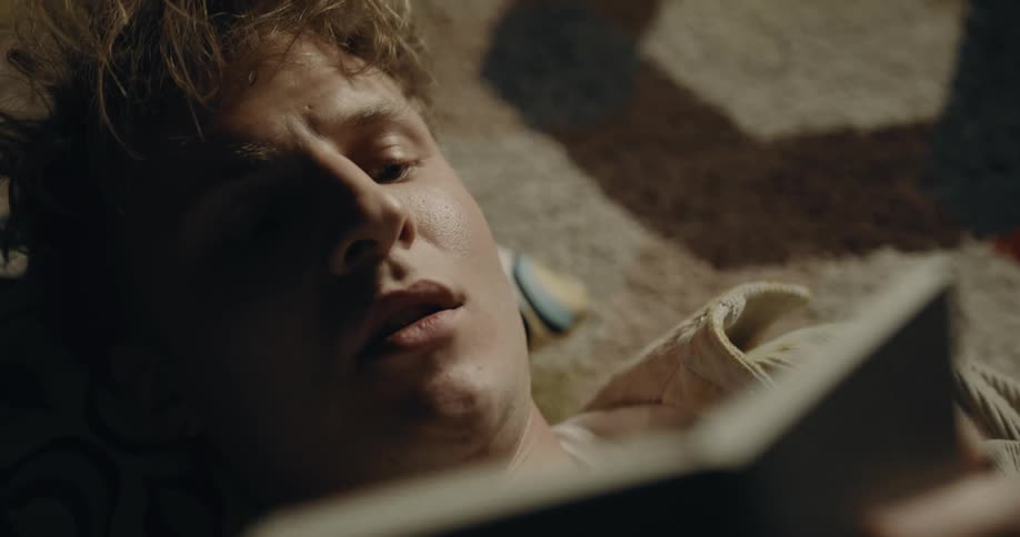 A man writing in a notebook while lying on a rug indoors
