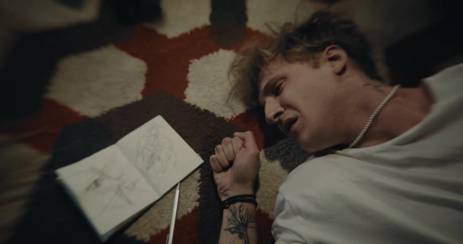 Man lying on his back on the floor sadly looks at notebook
