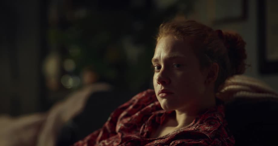 A woman with red hair in a ponytail sitting indoors on furniture