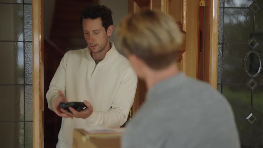 A man opens his front door and accepts a package from a delivery man
