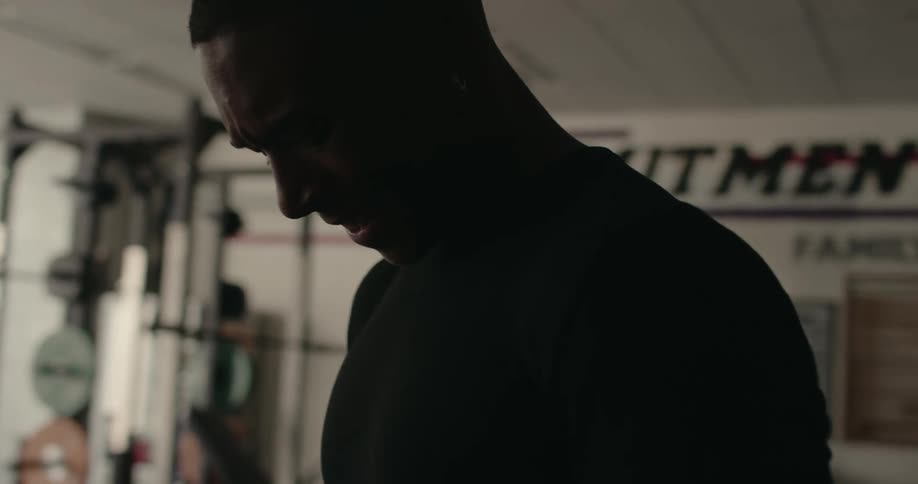 Closeup young black man wearing black tshirt doing alternating bicep curls in a weightlifting gym