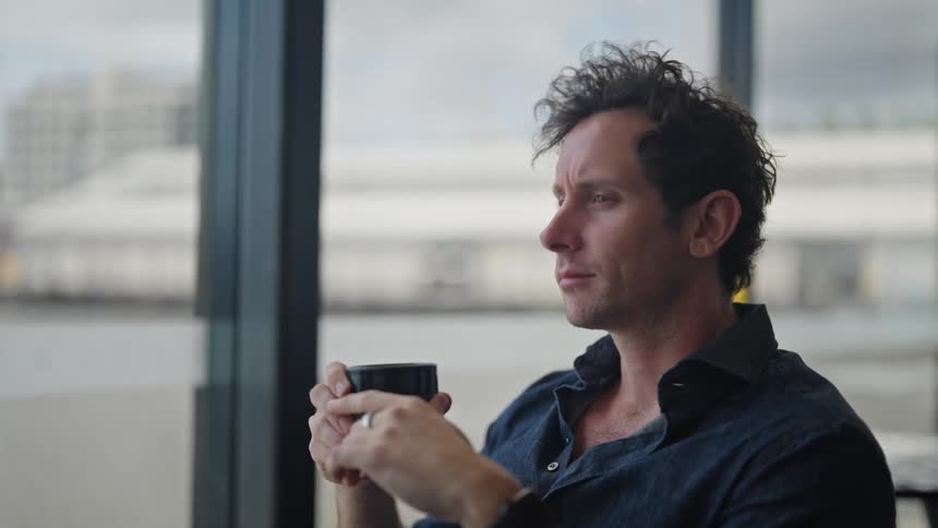 A man is sitting down and drinking a cup of coffee