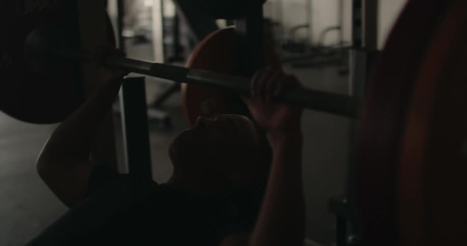 Black man in gym leans back onto weight bench and grips bar in preparation to do bench presses