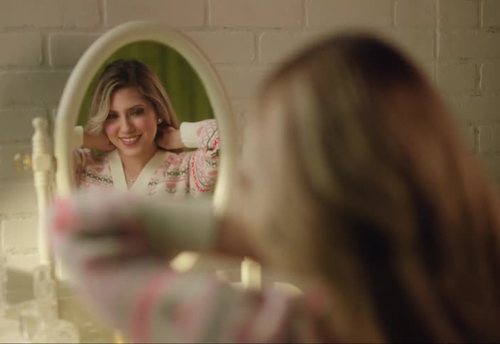 A woman is looking in a mirror and putting on jewelry