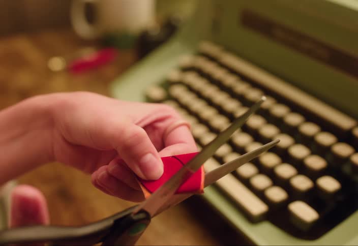 Woman cuts out heart from red paper near manual typewriter
