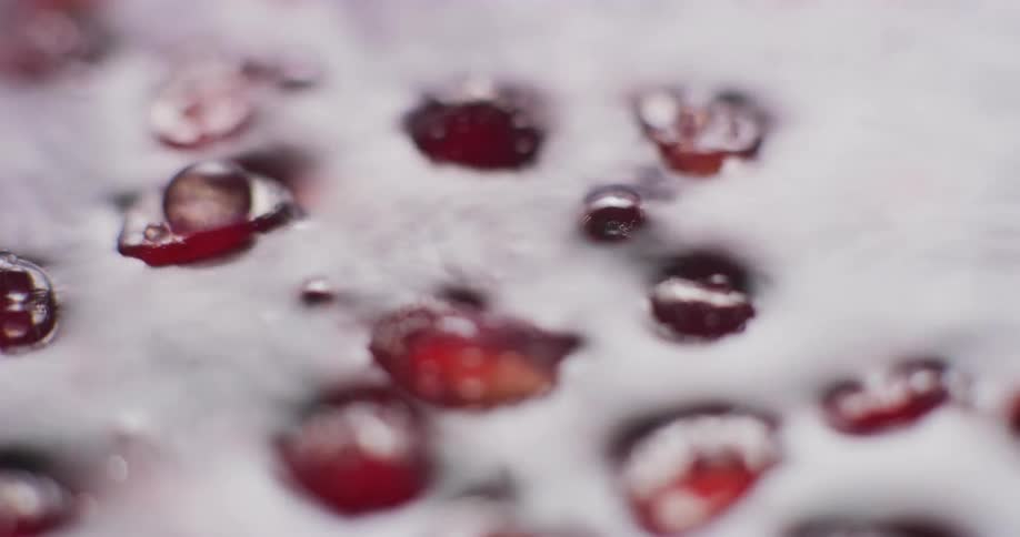 Bubbles move across surface of trembling water among floating pomegranate seeds