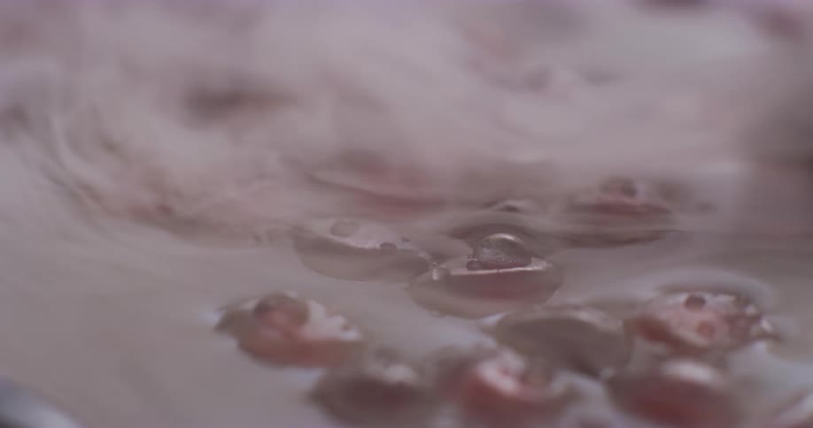 Closeup red pomegranate seeds with condensation floating in liquid with steam rolling over