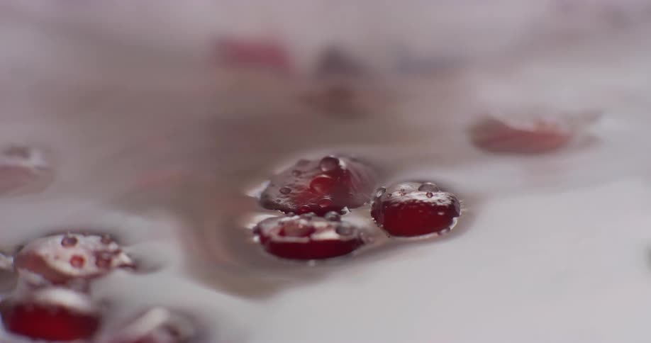 Cu a few red pomegranate seeds with condensation floating in water or juice and steam coming off
