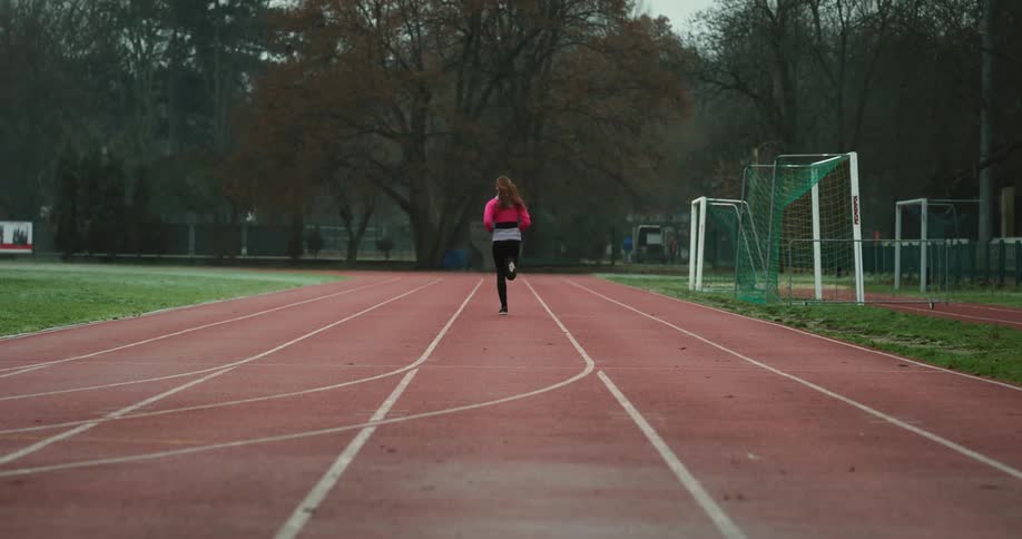 Woman starts from starting line and runs along running track while exercising