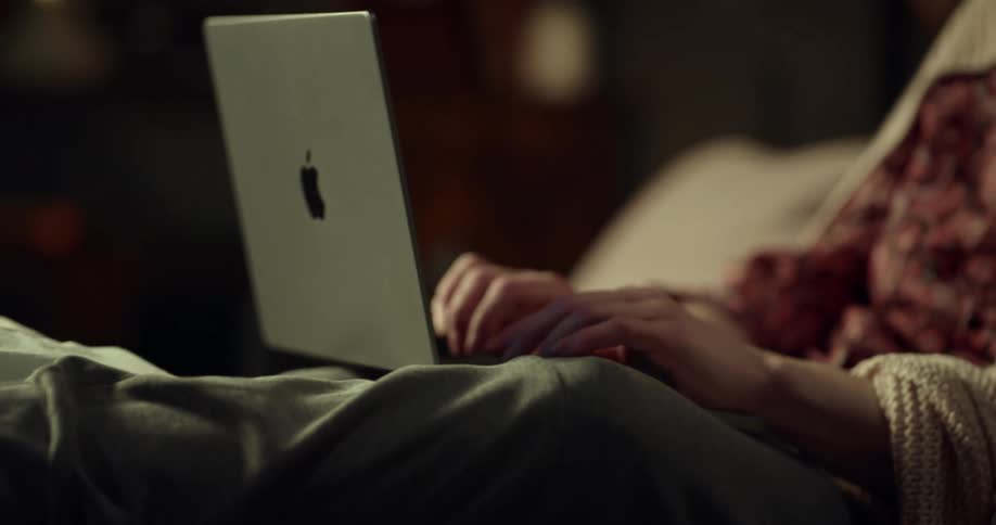 Woman typing on apple laptop looks at ankle propped on pillow topped with ice pack