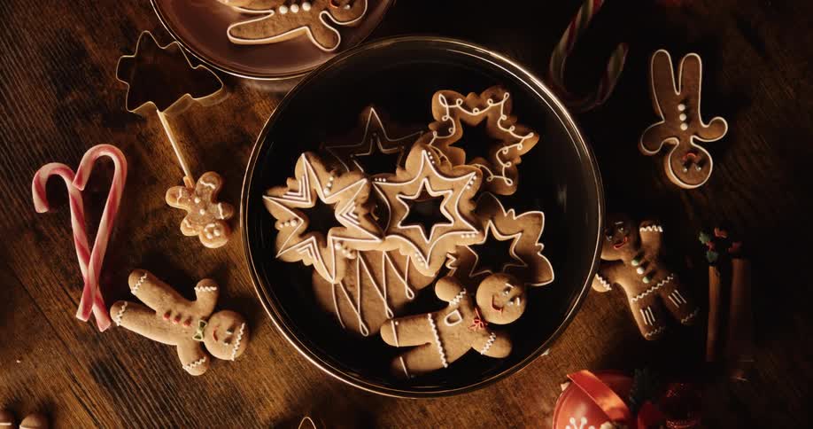 Trays of holiday gingerbread cookies are on a table with candy canes and cookie cutters