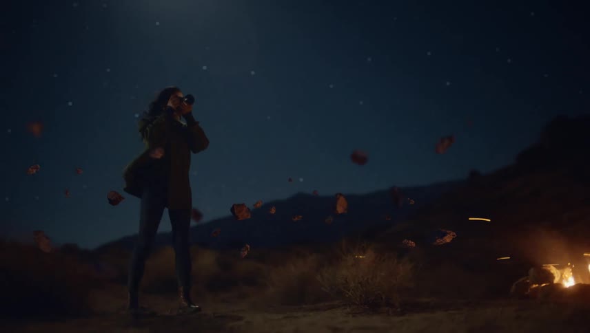 A woman is taking pictures of floating rocks around a campfire