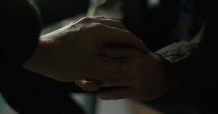 One persons hands are shaking as they are clasped together as another person places their hand on top of them and they hold hands