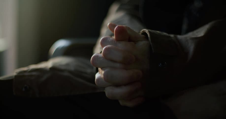 A person clinches their hands together while sitting in a chair indoors