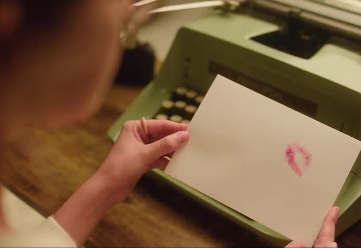 Woman sitting in front of manual typewriter kisses paper leaving a lipstick mark