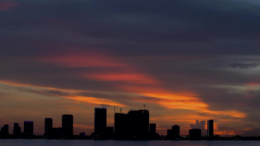 Vibrant red sky fades leaving skyscrapers near water silhouetted of Miami, Florida
