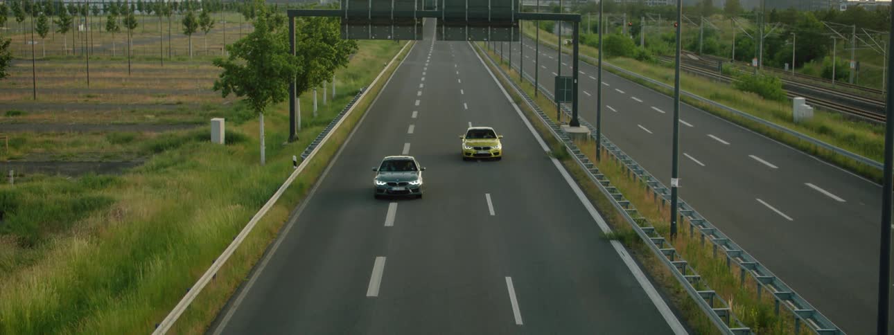 Two cars drive down controlled access highway away from buildings in the background