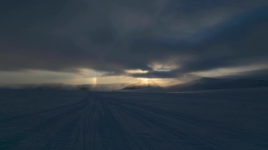 Clouds pass over a snow covered flatland in the North Pole during the day at sunset