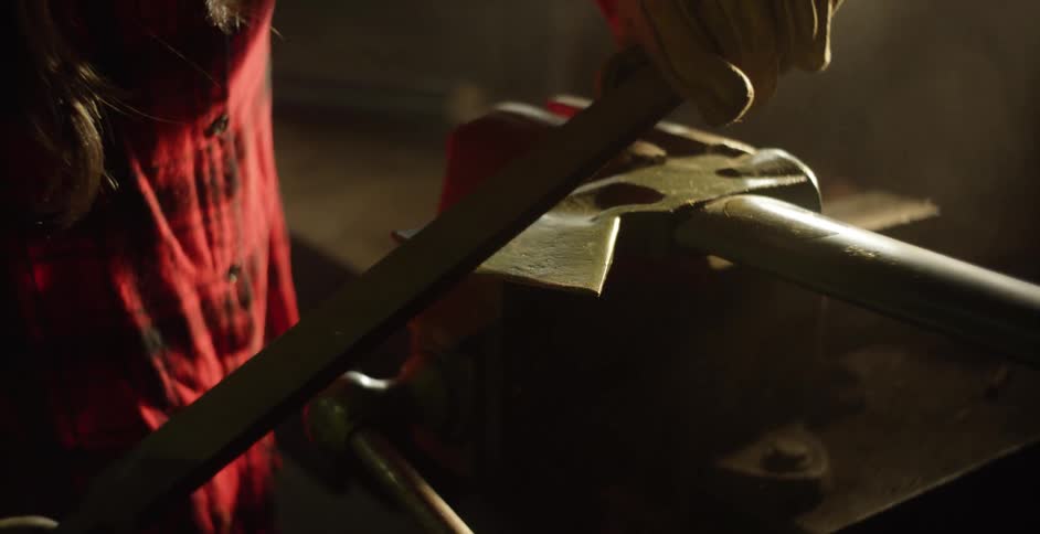 A man sharpens an ax in his workshop