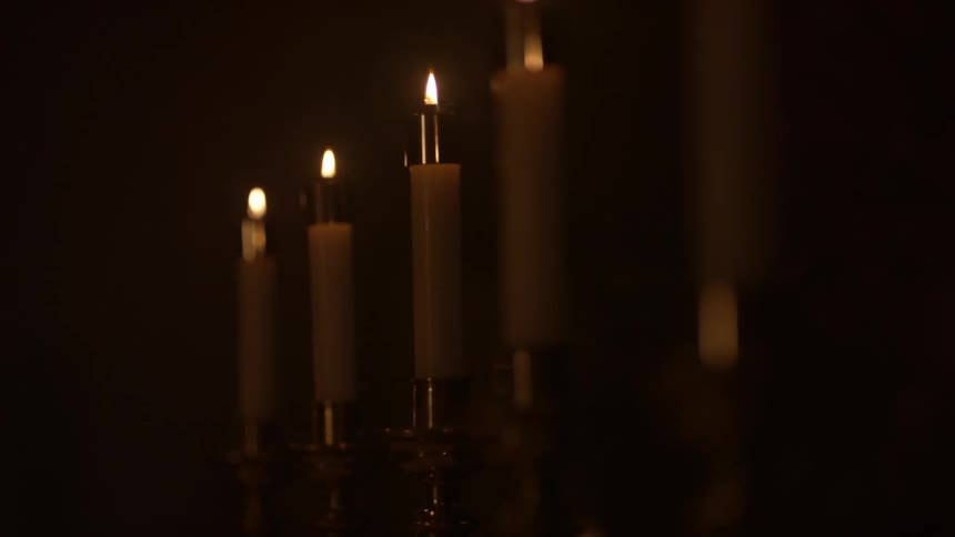 A row of candles burn in a dark room