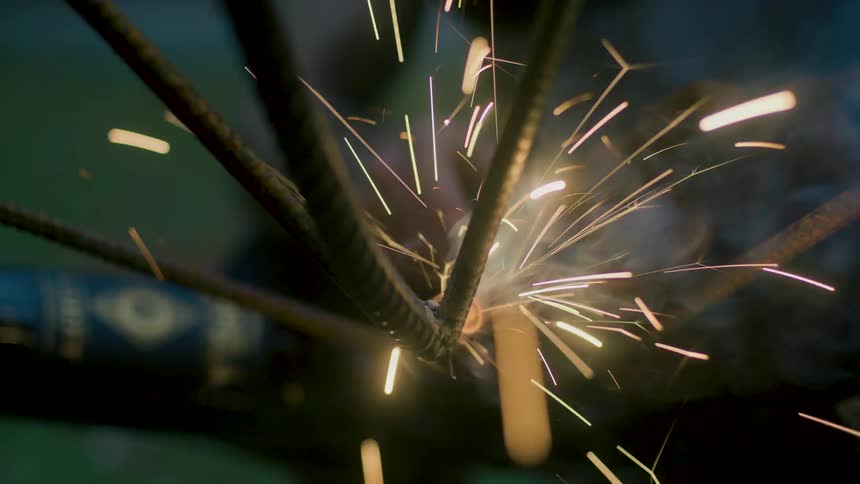 Sparks and smoke fill area as person welds multiple rebar bars