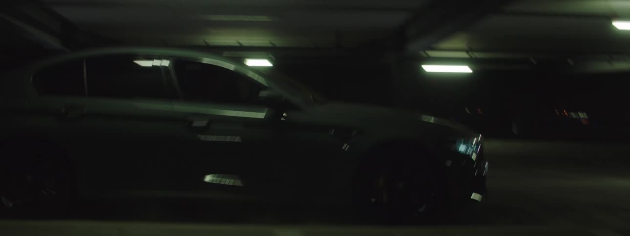 Two cars drive side by side through parking garage at night