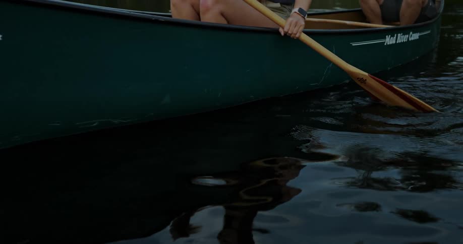 A man and a woman are holding their oars as they row a canoe across the river