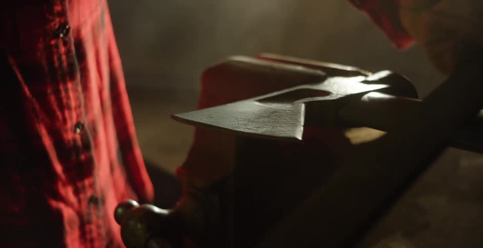 Man with red shirt sharpens an ax