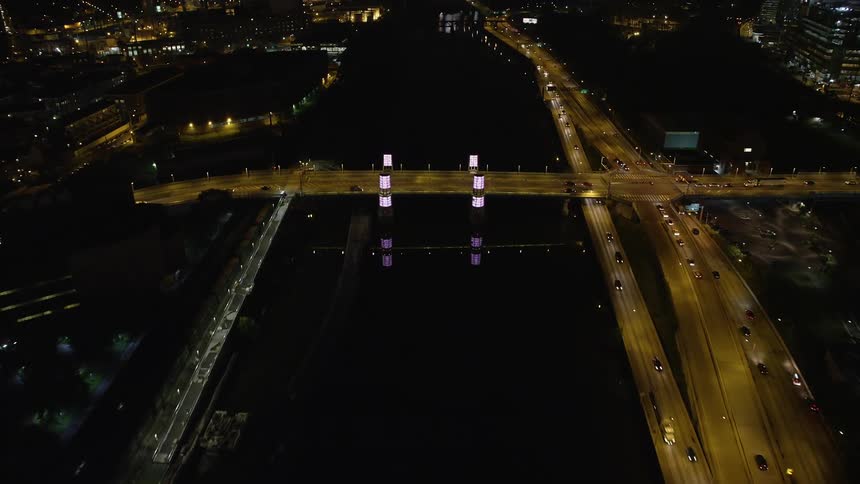 Approaching and tilting down to South Street Bridge over Schuylkill River at night capturing the reflection of the city lights and light traffic passing on the interstate highways