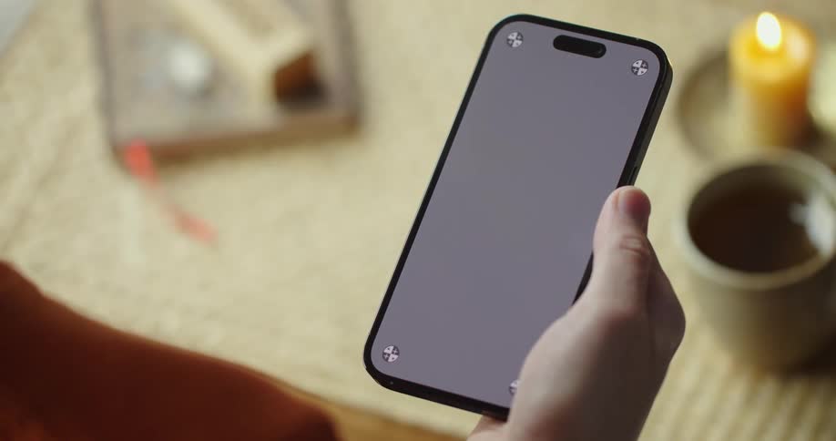 An up close of a persons phon with they scroll with their thumb in front of a table with a candle on it
