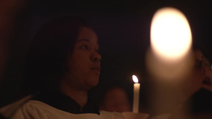 A woman holding a candle as she sings with a choir