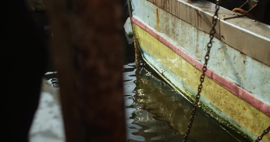 Water reflects boat floating in water moored with a chain near dock
