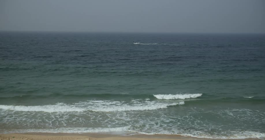 Boat moves across ocean in distance as waves crash onto beach