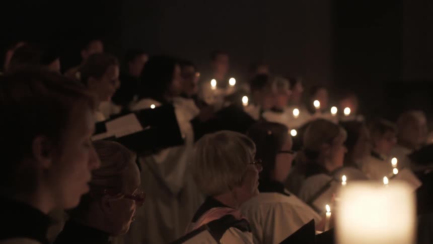A choir holding candles as it performs by candlelight