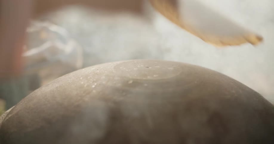 Daytime a woman making armenian lavash bread on a makeshift outdoor woodburning stove burning twigs underneath steam and smoke coming off