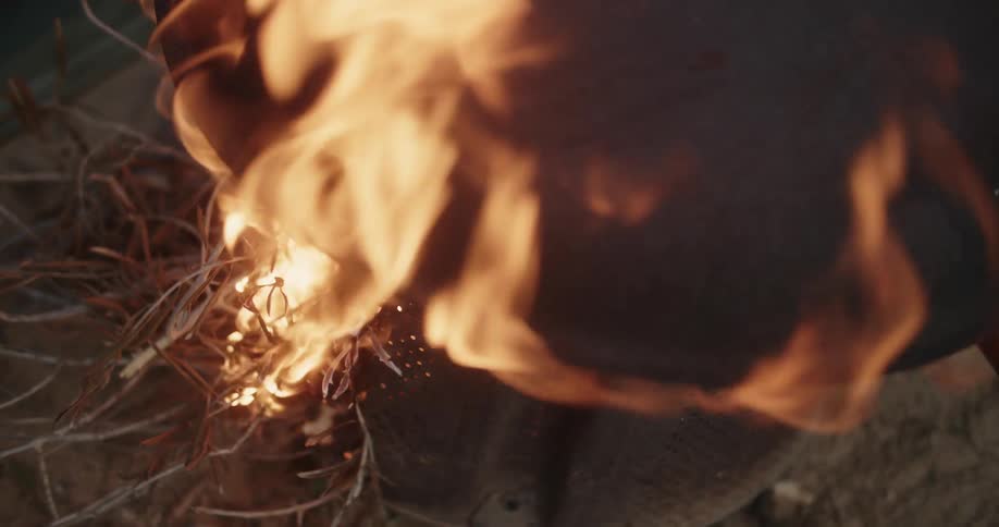 Flames are rising and wavering as fire is burning dry weeds with a pot on top