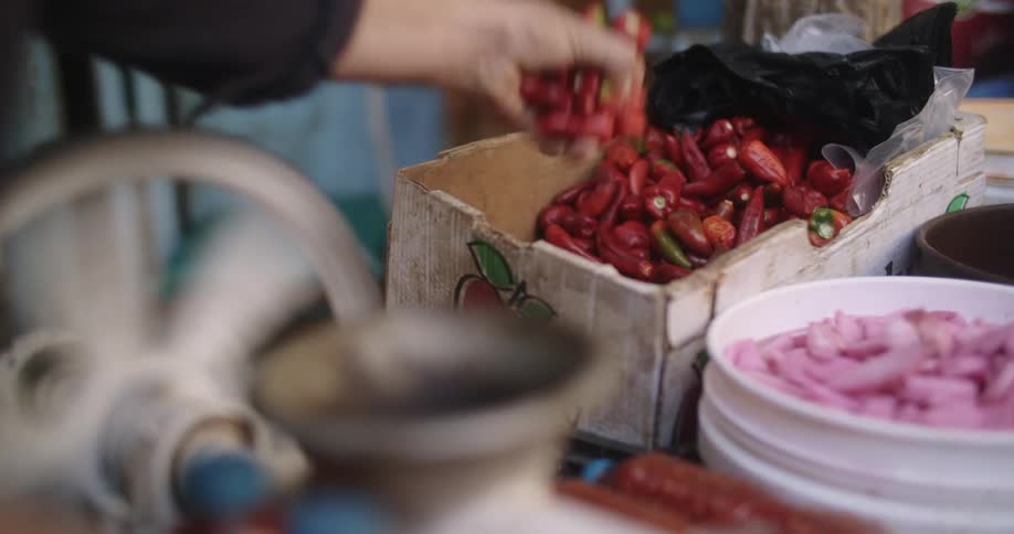 A person is loading red peppers into a processing machine while indoors during the day