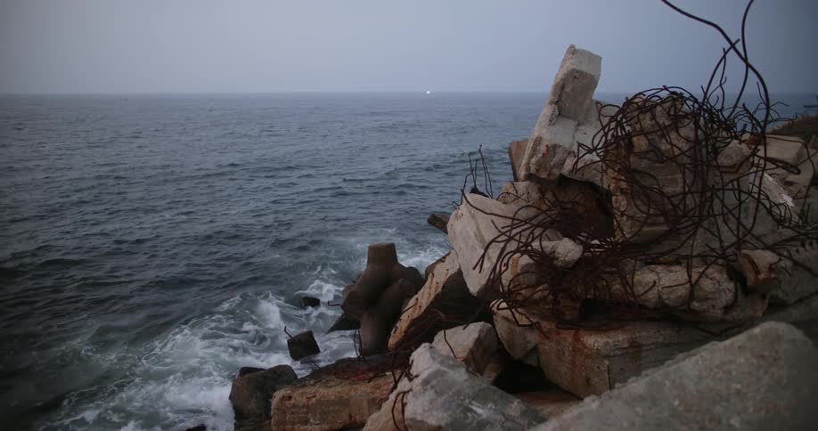 Waves crash against breakwall made from large uneven blocks