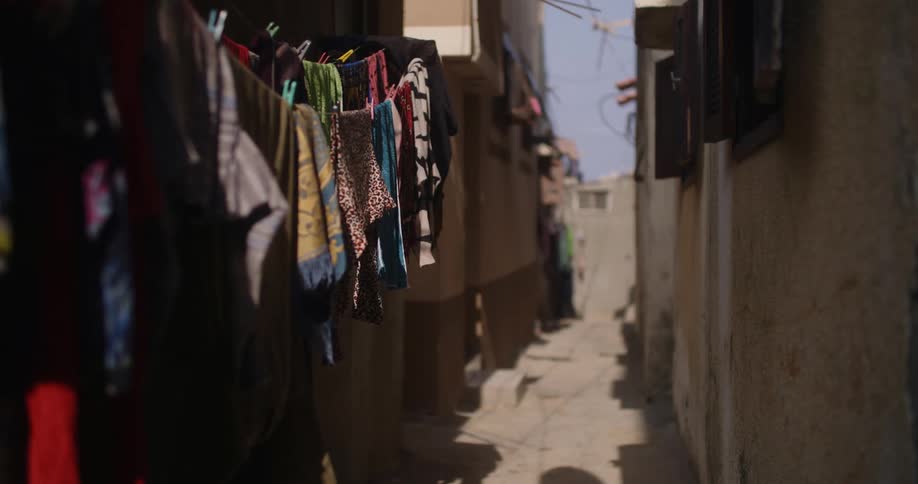 Clothes swing on clothesline in alley as pedestrians cross at end of block