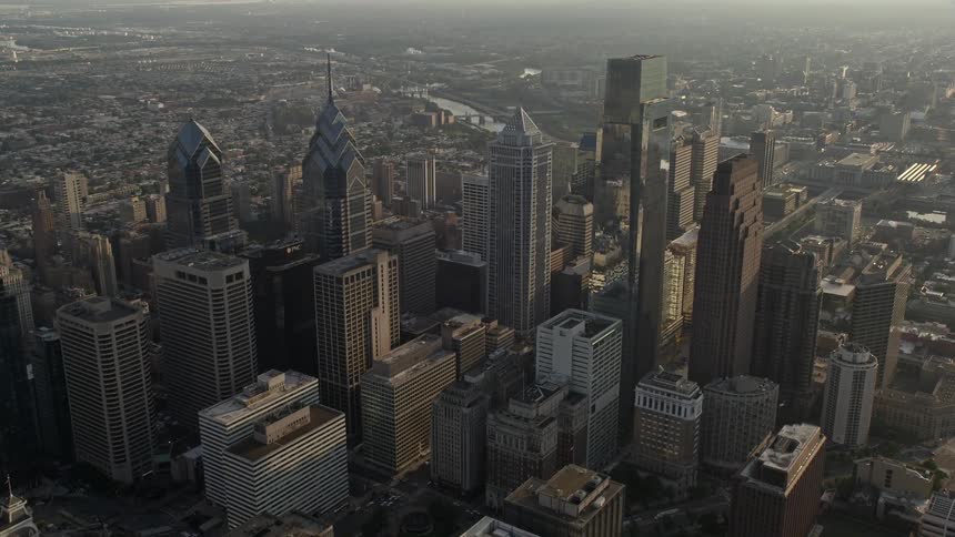 Approaching Philadelphias City Hall and downtown skyscrapers during sunset towering over the historical city with a hazy view of the river nearby