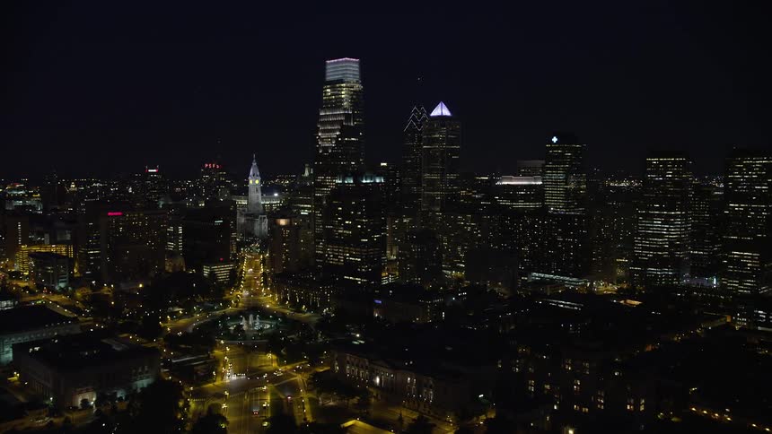 A nighttime aerial view of Philadelphias city streets and skyline with glowing lights approaching City Hall and Downtown on Benjamin Franklin Parkway