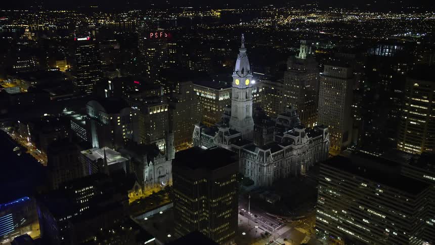 An aerial approach and orbit of Philadelphia City Hall in Downtown Philadelphia at nighttime showcasing the iconic landmark and historic government building